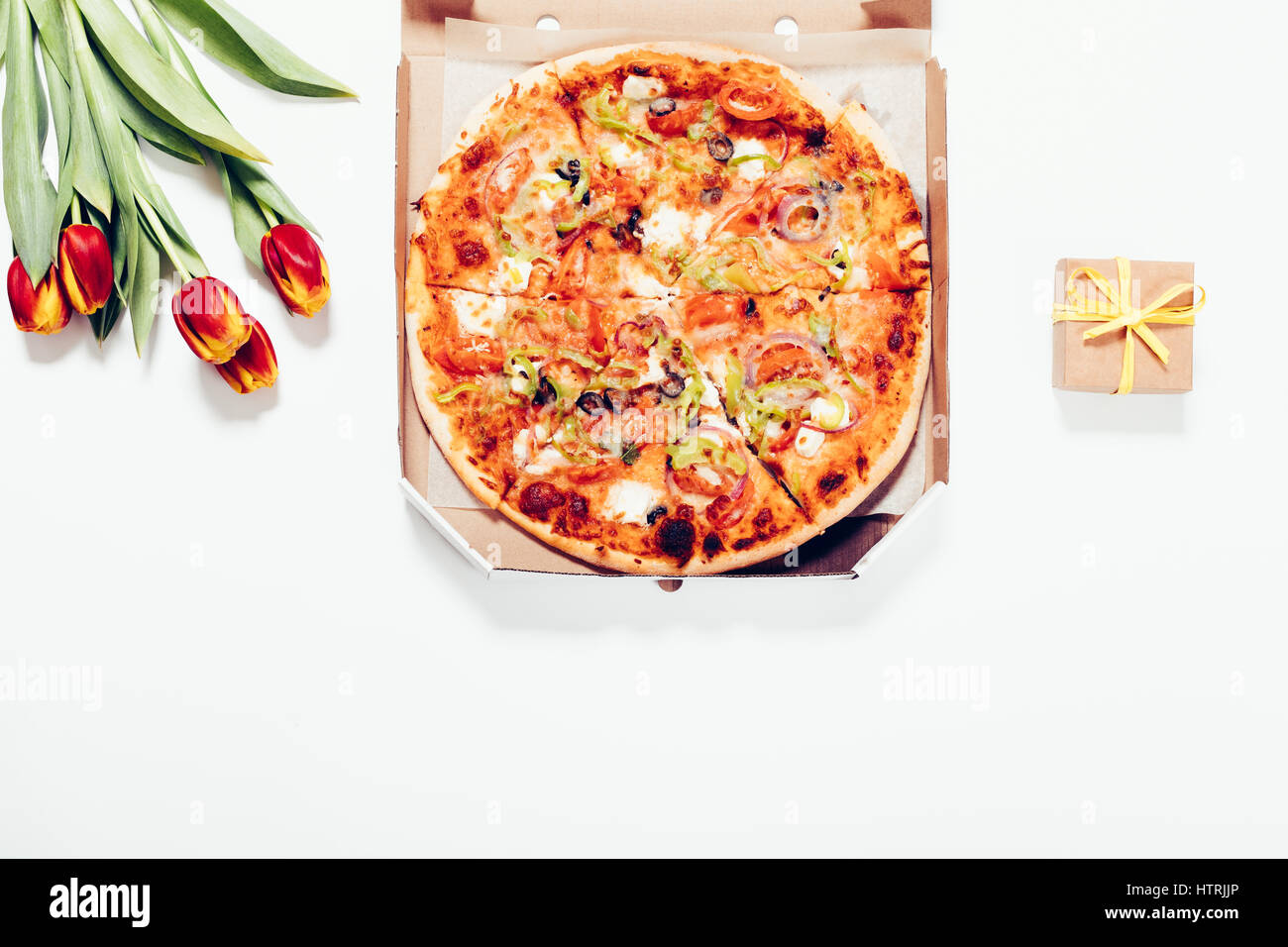 Pizza in einer Box, roten Tulpen und ein kleines Kästchen mit einem Geschenk auf einem weißen Hintergrund, Ansicht von oben Stockfoto