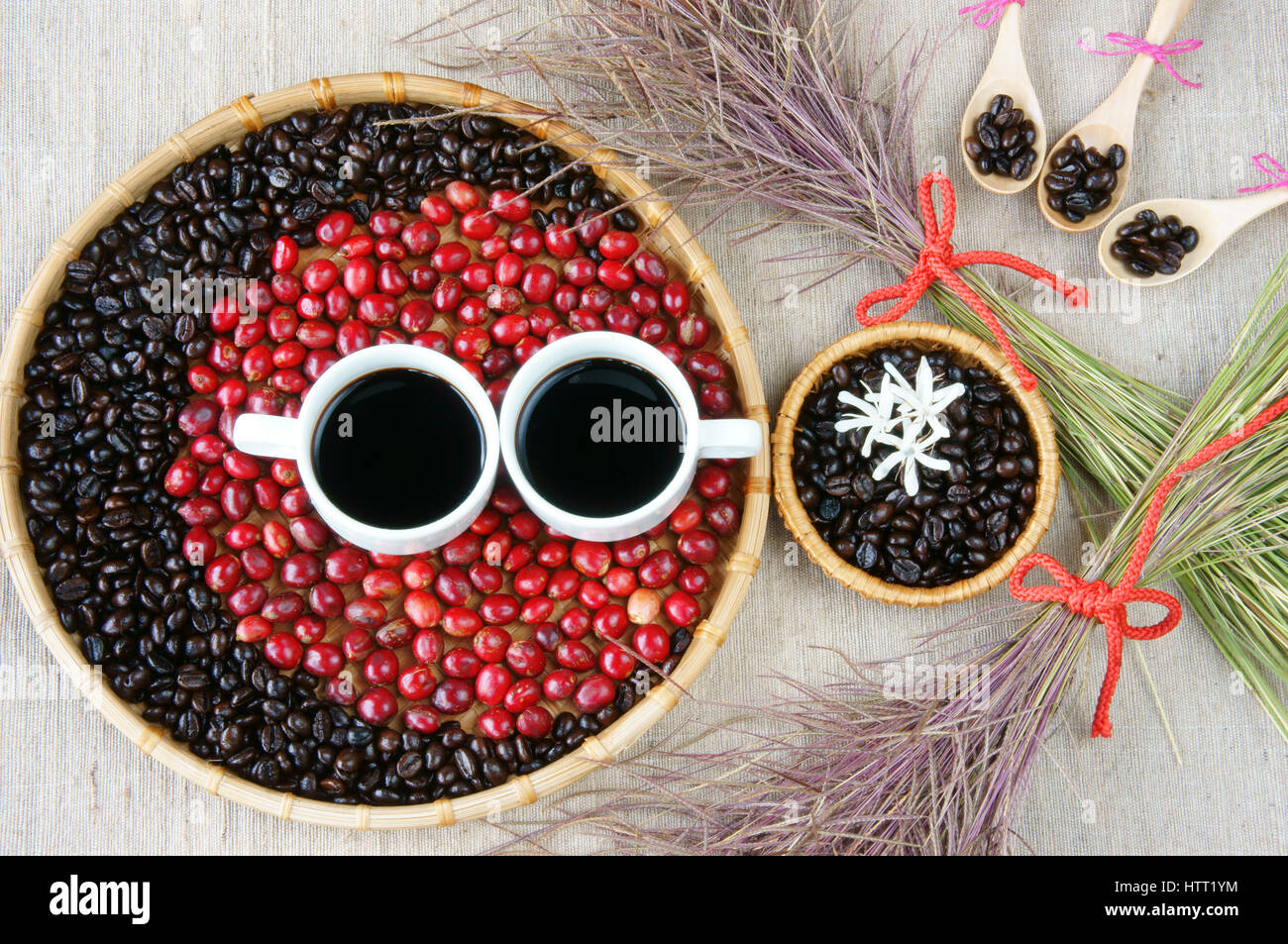 Sammeln von Café Samen, roten reifen Beeren, gerösteten Kaffee Bohnen, Kaffee, Holzlöffel, weiße Blume auf Bambuskorb, Sackleinen Hintergrund, Wirtschaft Stockfoto