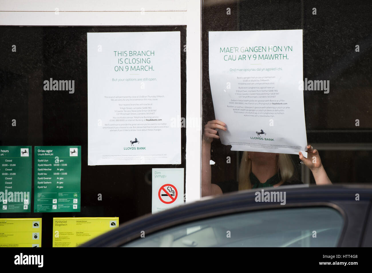 Lloyds Bank schließt seine Niederlassung in einem kleinen walisischen Stadt: 9. März 2017 - ein Frau-Mitarbeiter stellt Informationen im Fenster der Zweig der Lloyds Bank, am Nachmittag geschlossen für das gute, in der kleinen ländlichen Tregaron Dorf Ceredigion Wales UK Stockfoto