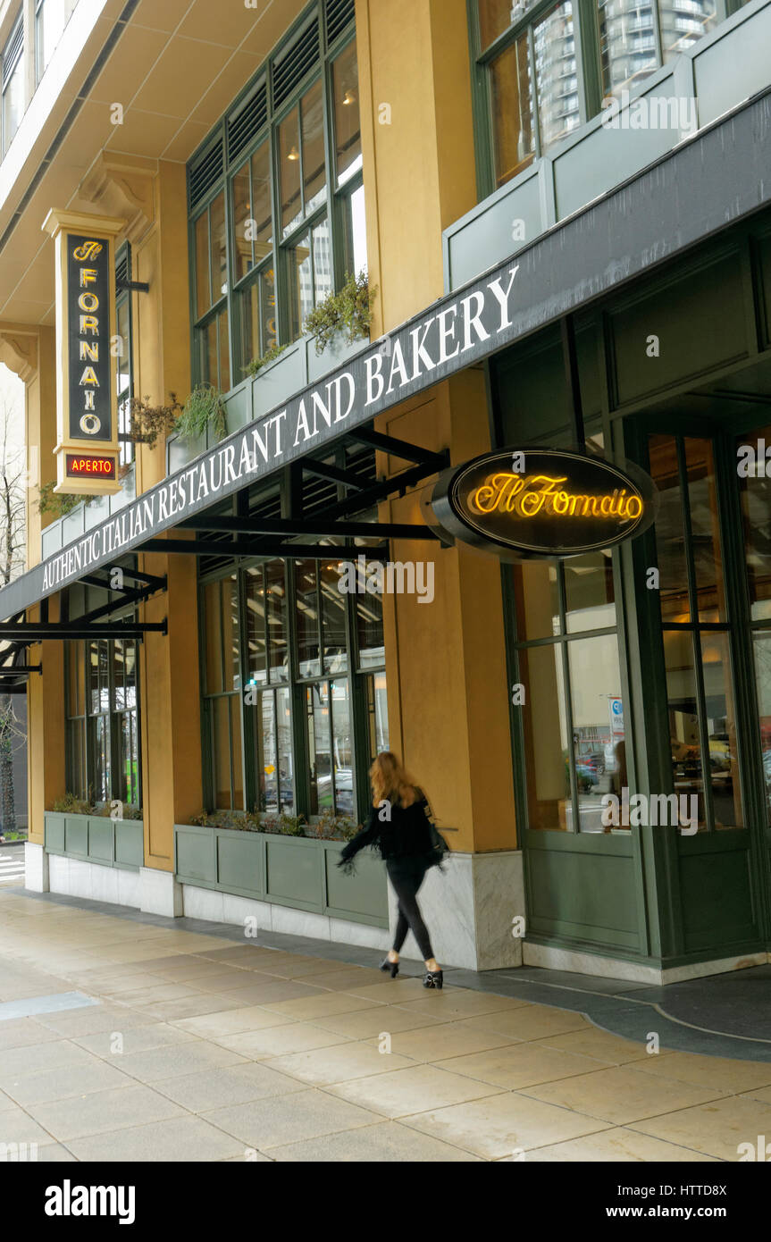 Stilvoll gekleidete junge Frau zu Fuß durch Il Fornaio italienisches Restaurant und Bäckerei in der Innenstadt von Seattle, Washington, USA Stockfoto