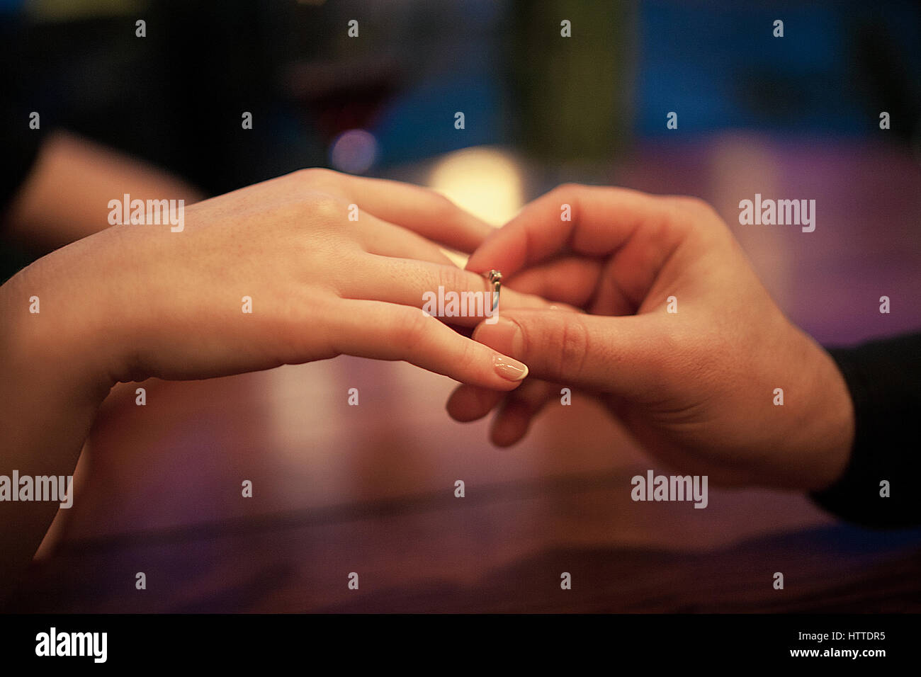 Junger Mann macht Frau Heiratsantrag und setzt ein Engagement ring an ihrem Finger. Hautnah. Sie sitzen am Tisch. Stockfoto