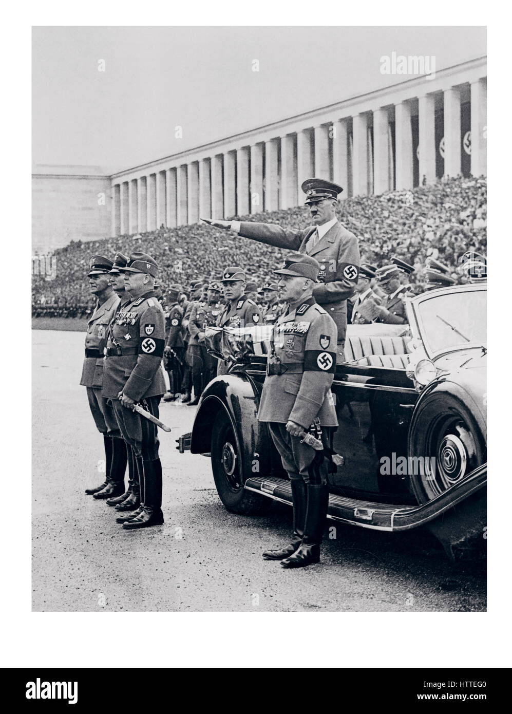 NÜRNBERGER KUNDGEBUNG 1930er-Kanzler Adolf Hitler in Uniform mit Hakenkreuzarmband, stehend in seinem Mercedes-Auto, grüßend Mitglieder des Arbeiterkorps, während sie während einer Überprüfung auf Nürnberg Zeppelin Feld, Teil der Zeremonien des jährlichen Nazi-Parteikongresses marschieren. Stockfoto