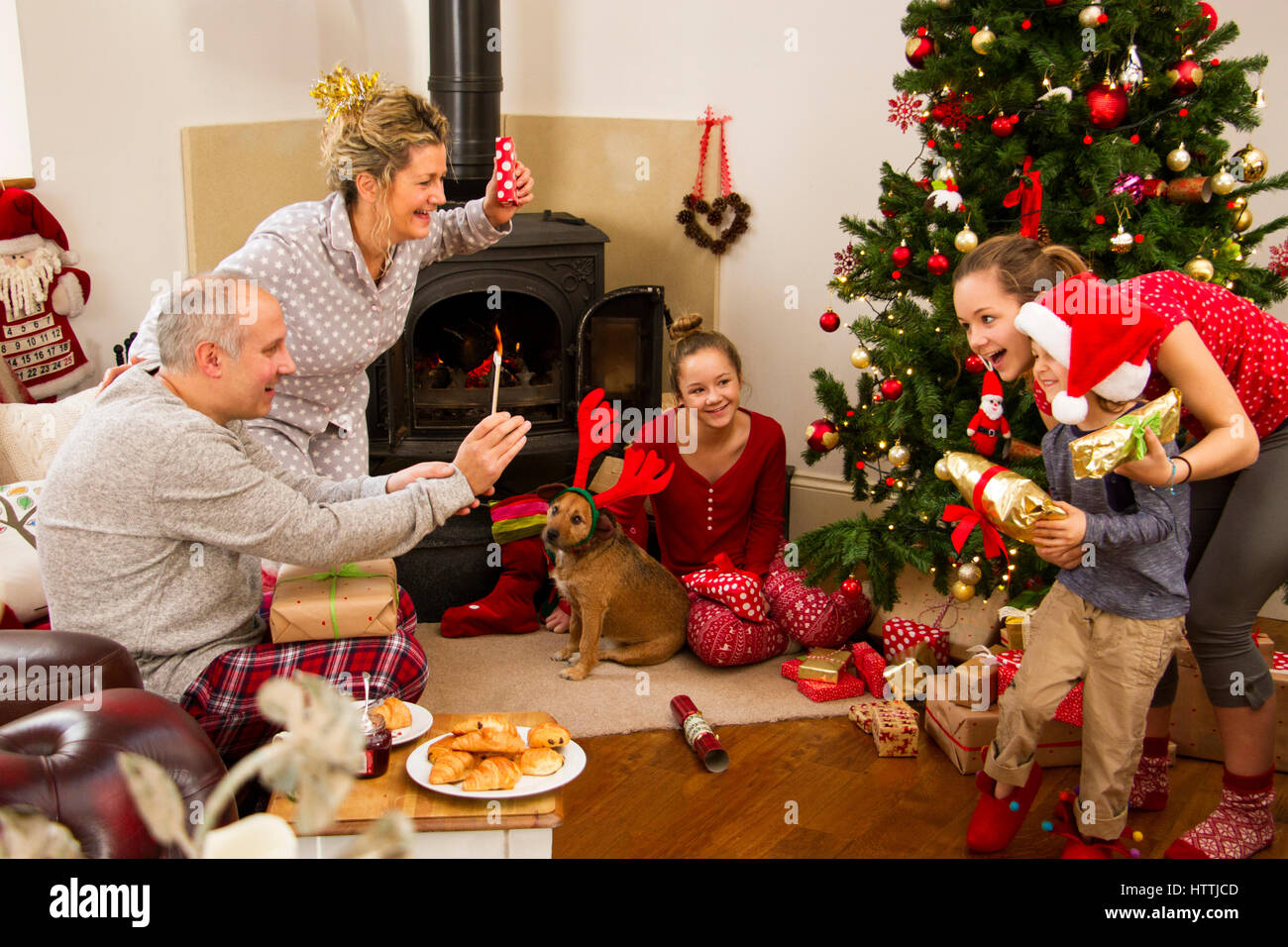 Familie genießen ihren Weihnachtsmorgen. Der Vater ist ein Smartphone verwenden, nehmen Sie ein Foto von zwei seiner Kinder. Die Mutter und eine der Schwestern ar Stockfoto