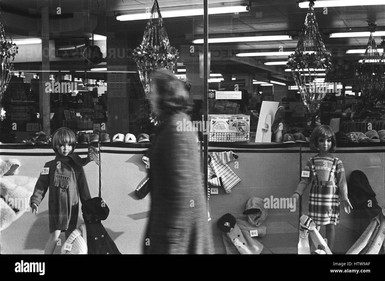 Archiv Bild eines weiblichen Shopper vorbei Weihnachten Anzeige von Kinderbekleidung in einem Kaufhaus Schaufenster, Lambeth, London, England, 1979, Bewegungsunschärfe Stockfoto