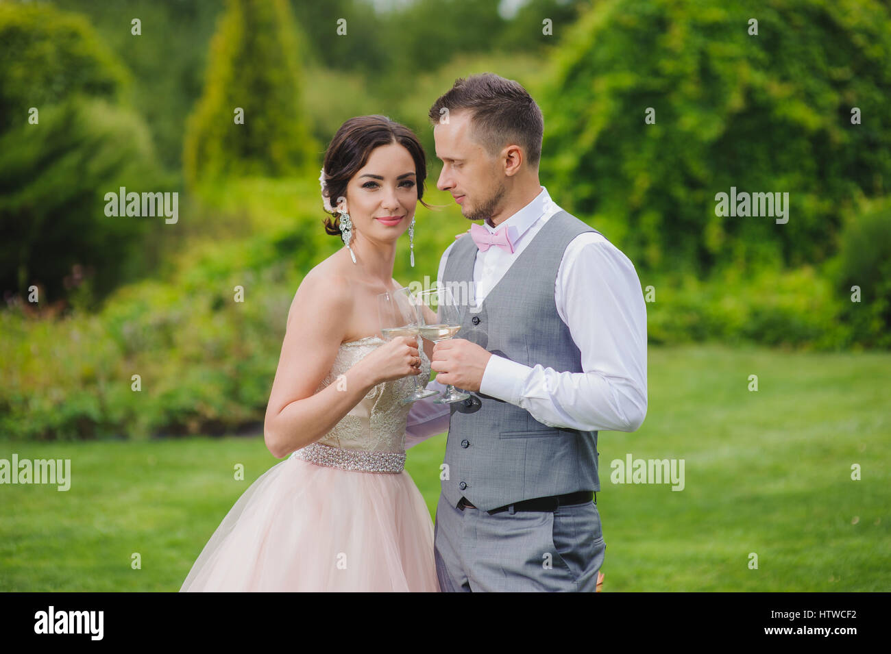 Klirrende Gläser. Braut und Bräutigam machen Toast. Durchschnittliche Plan. Grass, Ballen Heu Bäume und Büsche im Hintergrund. Stockfoto