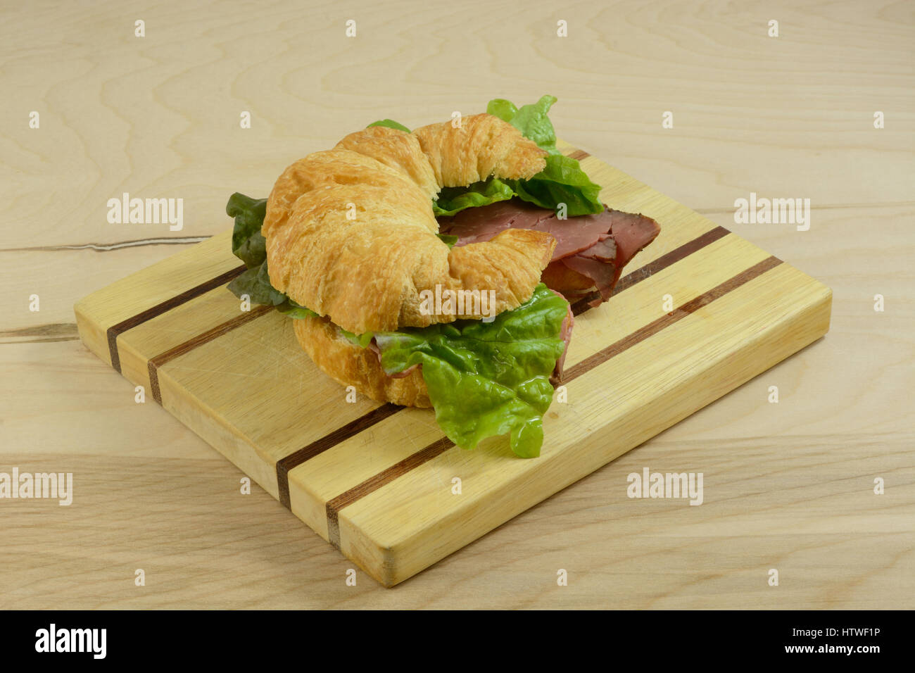 Gebratenes Rindfleisch Croissant Sandwich auf Schneidebrett Stockfoto