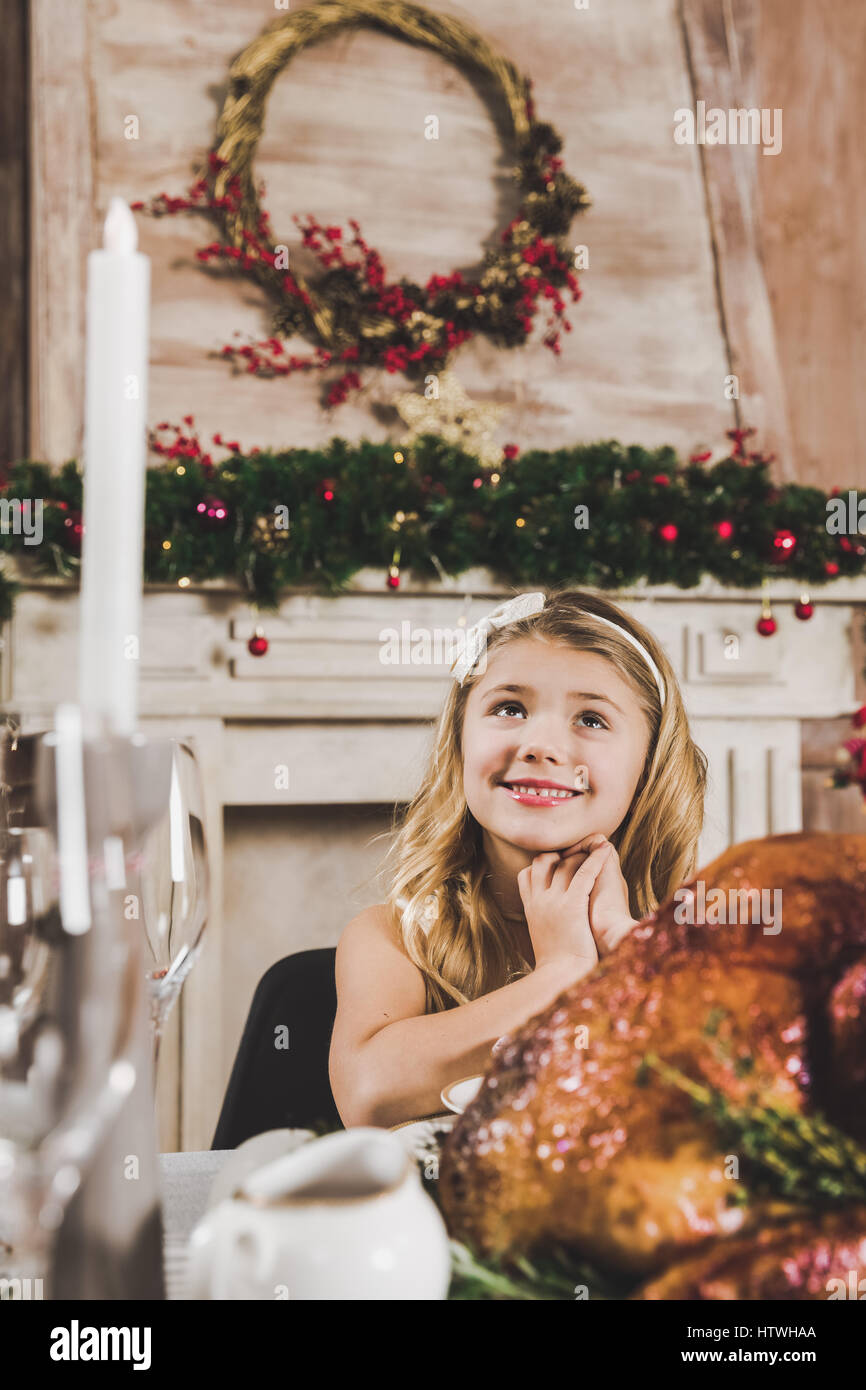 Niedliche lächelndes Mädchen am Urlaub Tisch sitzen und das Nachschlagen in der Weihnachtszeit Stockfoto
