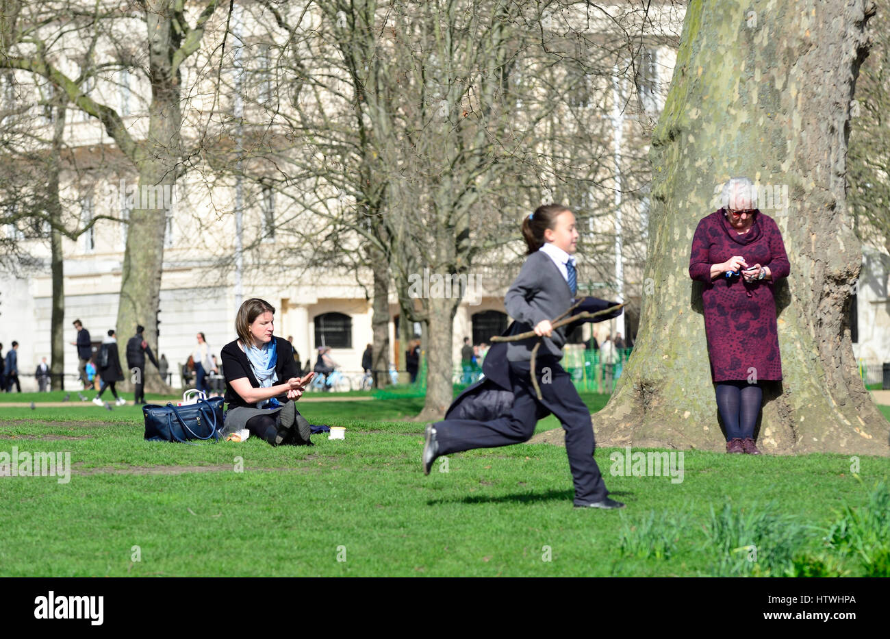 London, Großbritannien. Drei Generationen von Frauen im St. James' Park, zwei ältere mit Handys und ein junges Mädchen mit einem Stock Stockfoto