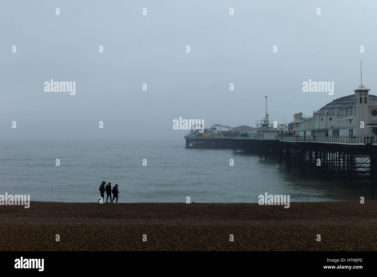 Drei junge Leute, die zu Fuß am Strand im frühen Morgennebel durch Brighton Pier Stockfoto