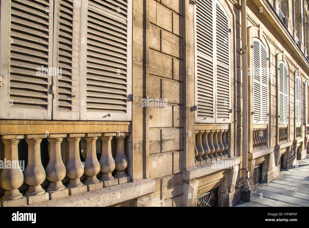 Geschlossenen weißen Fensterläden auf vasenförmige Geländerstäbe werden erwärmt durch den späten Tag Sonnenlicht auf ein altes Gebäude in Paris Frankreich. Stockfoto