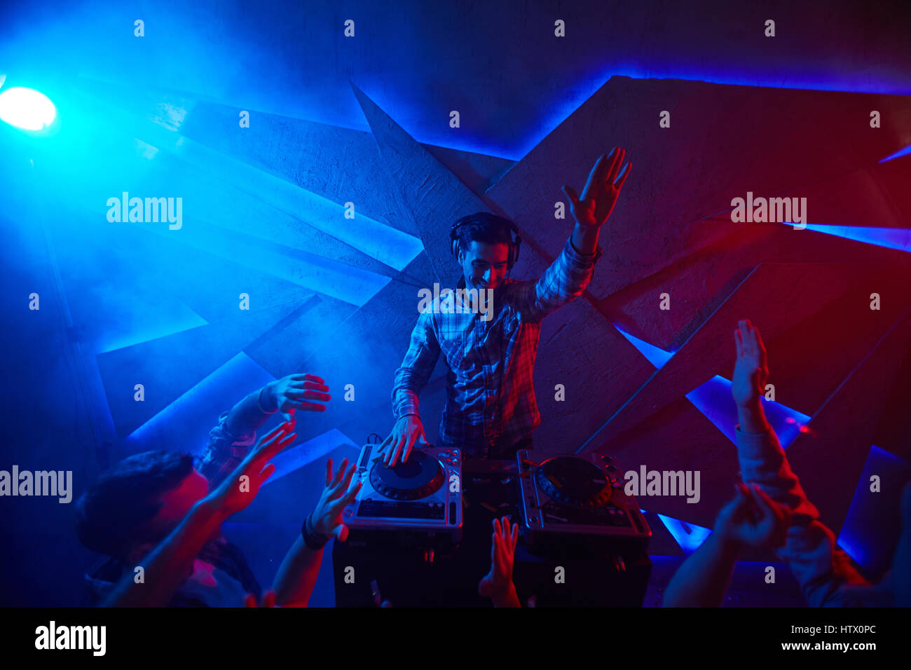 Junger Mann mit erhobener Hand unterhaltsam begeistert Publikum im Disco-club Stockfoto