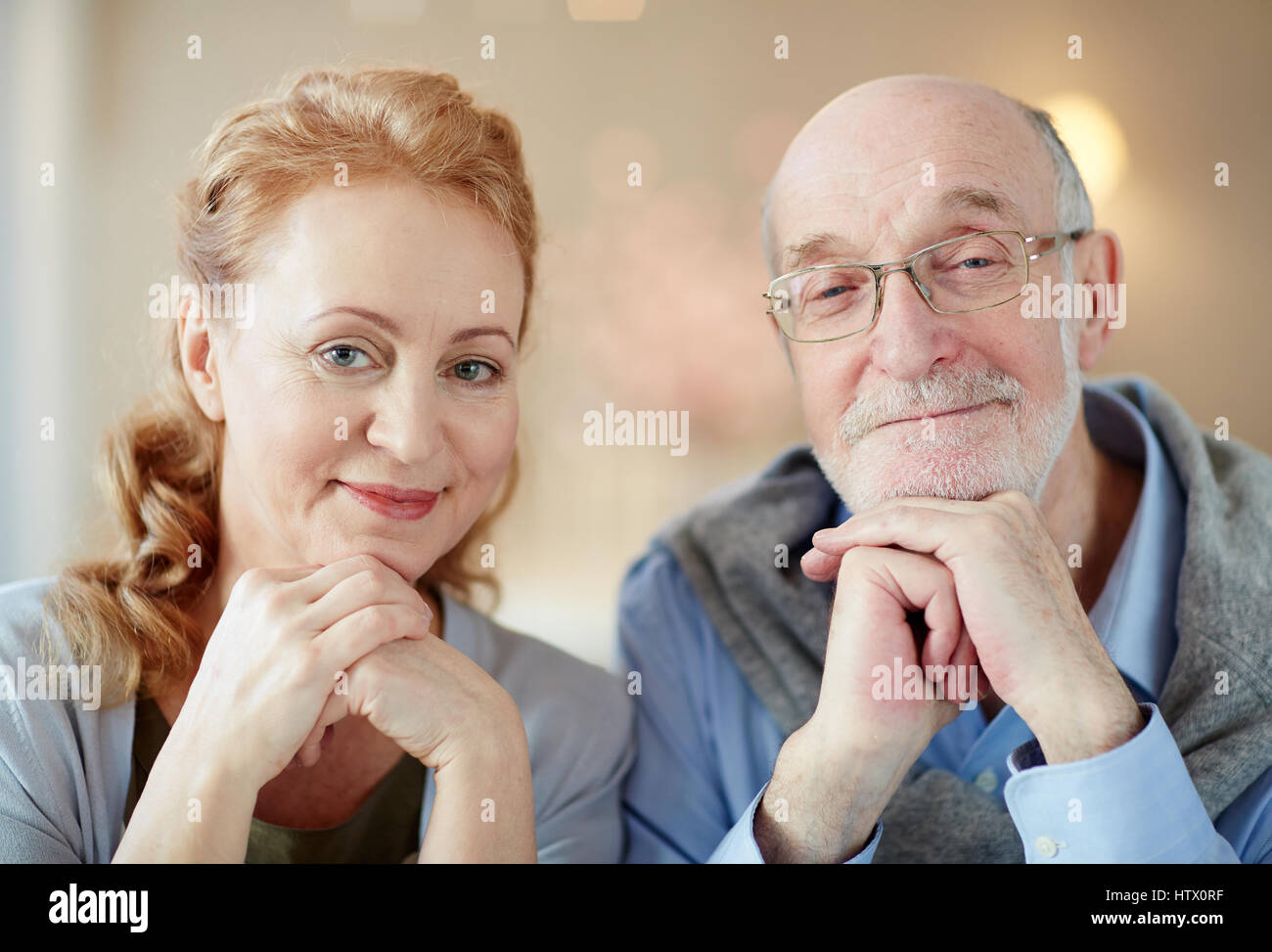 Porträt von nett lächelnd älteres paar zu Hause, graue dunkelhaarigen Mann und elegante ältere Frau Blick in die Kamera ruht Kopf auf Händen Stockfoto