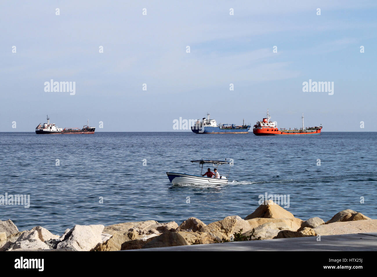 Ein kleines Boot hereinkommt zum Ufer entlang der Küste von Limassol, Zypern, mit großen Tankern und anderen Schiffen im Hintergrund. Stockfoto