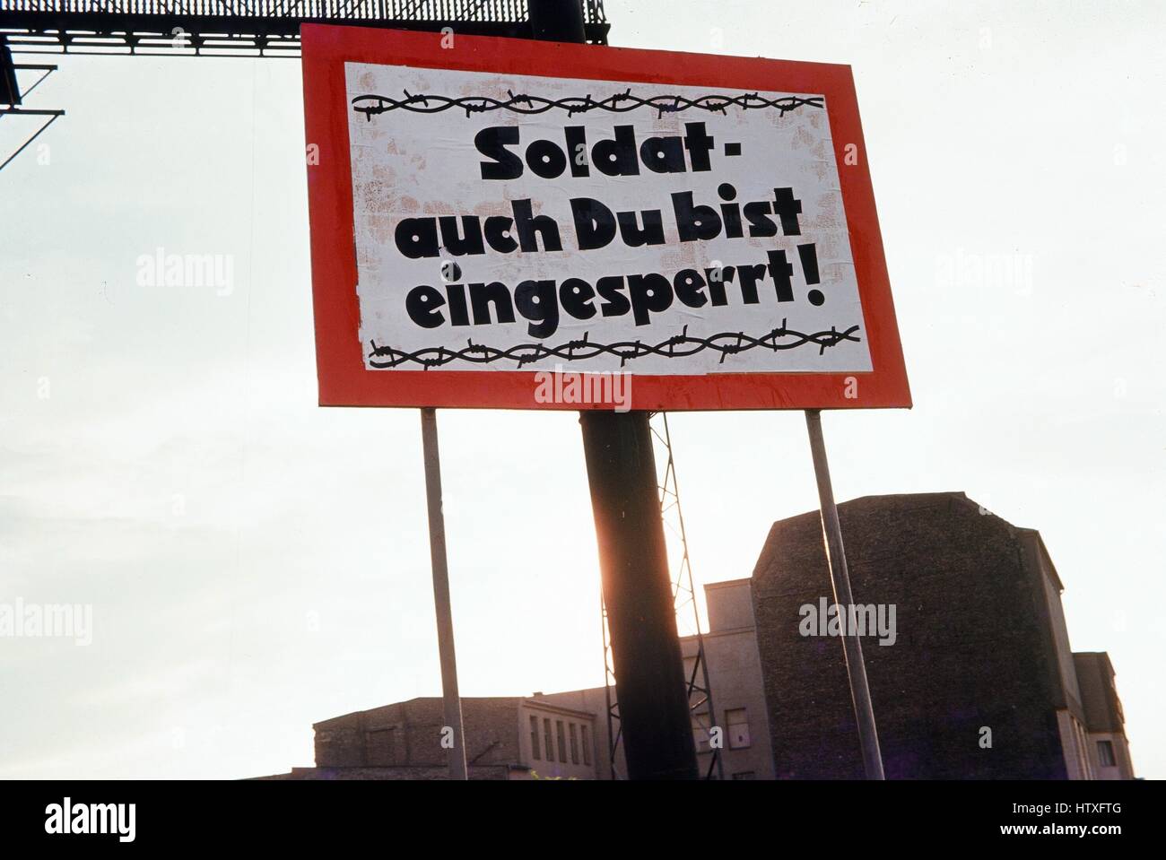 Roten und weißen Schild mit Stacheldraht Grafik an der Grenze zwischen West-Berlin und Ost-Berlin, während des Kalten Krieges, mit Text auf Deutsch lesen "Soldat Auch du Bist Eingesperrt" oder "Soldaten Sie auch gefangen sind", Förderung der ostdeutschen Soldaten in den Westen, Deutschland, 1975 defekt. Stockfoto