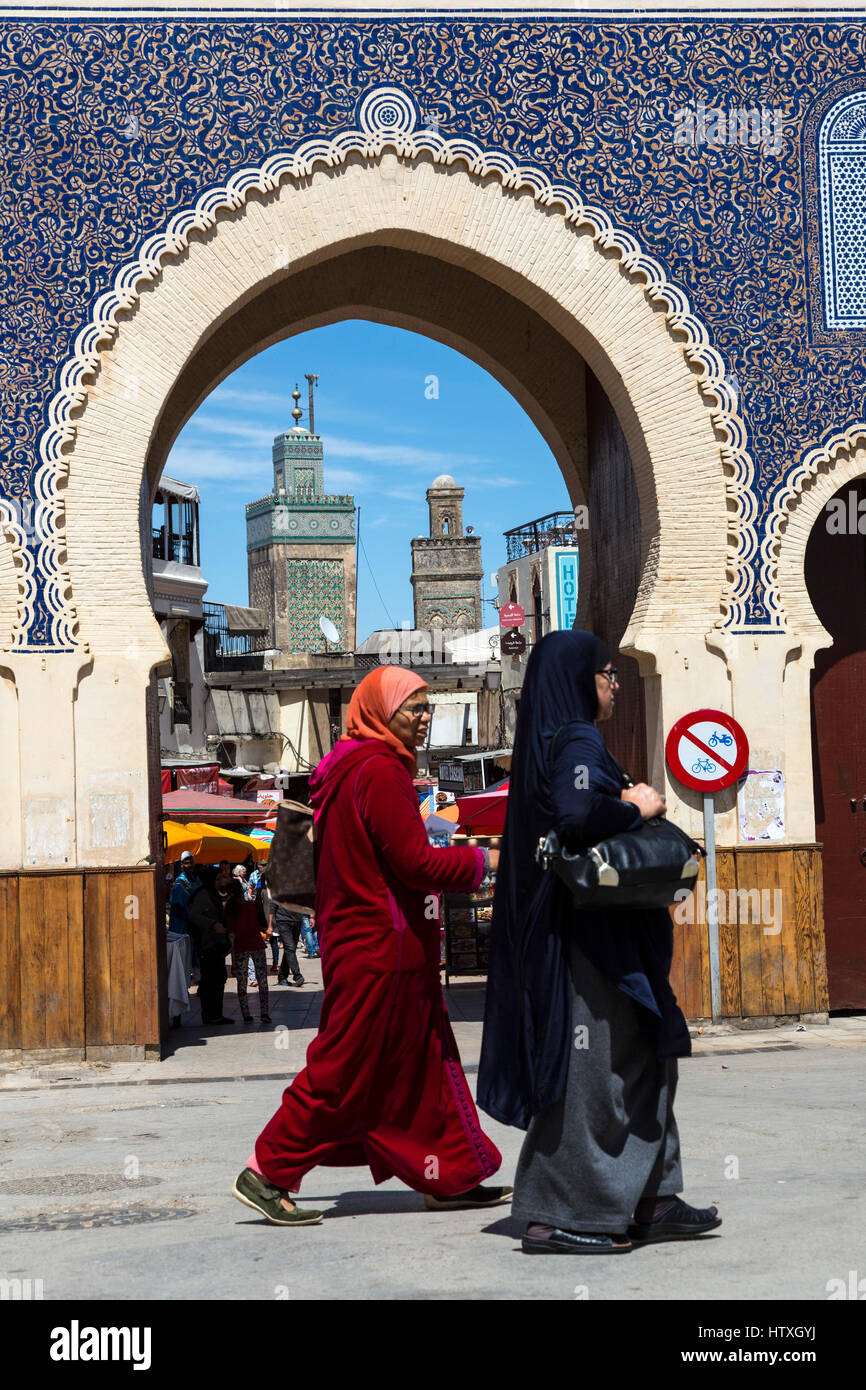 Fes, Marokko.  Zwei Frauen mittleren Alters gehen vorbei an der Bab Boujeloud, Eingang zum Fes El-Bali, der alten Stadt.  Das Minarett der Medersa Bou Inania ist in Stockfoto