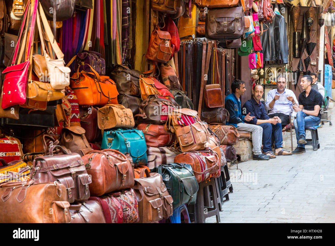 Fes, Marokko.  Straßenszene in der Medina.  Männer sitzen außen Shop verkauft Lederwaren. Stockfoto