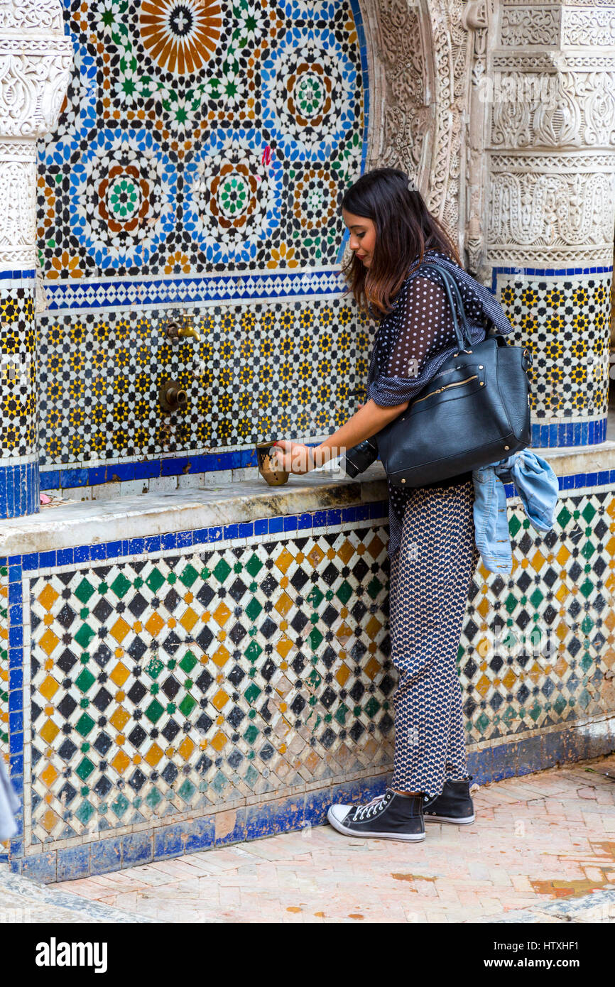 Fes, Marokko.  Nejjarine zu platzieren.  Junge Frau mit öffentlichen Trinkbecher am Brunnen. Stockfoto