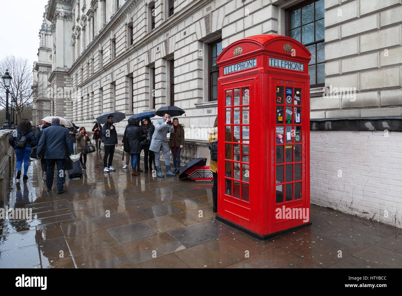 Touristen, die Aufnahmen vor einem alten London Telefon Box auf einem nassen und regnerischen Tag, Great George Street, SW1 Stockfoto