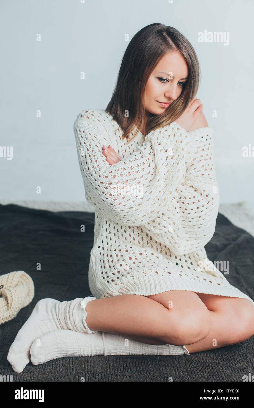 Frau in Strickpullover sitzt auf einem Bett Stockfoto