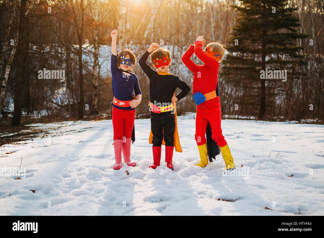 Drei Kinder stehen auf zugefrorenen See in Superhelden-Kostümen Stockfoto