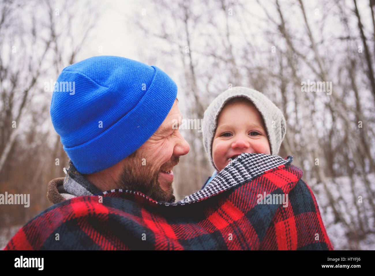 Porträt eines Vaters, der sein Kind in einem Winterwald in einer Decke gehüllt trägt Stockfoto