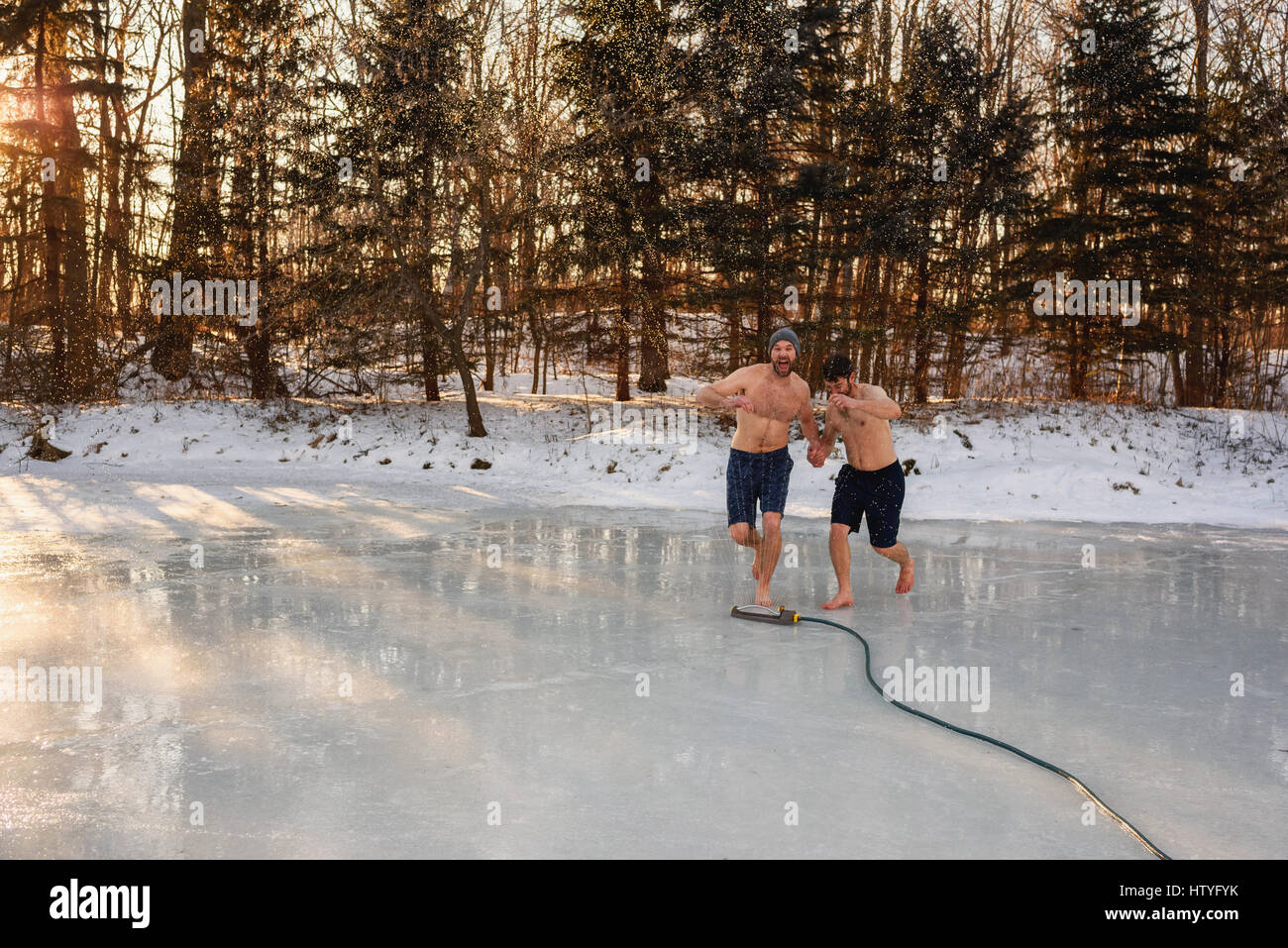 Zwei Männer in kurzen Hosen laufen durch Sprinkler auf zugefrorenen See Hand in Hand Stockfoto