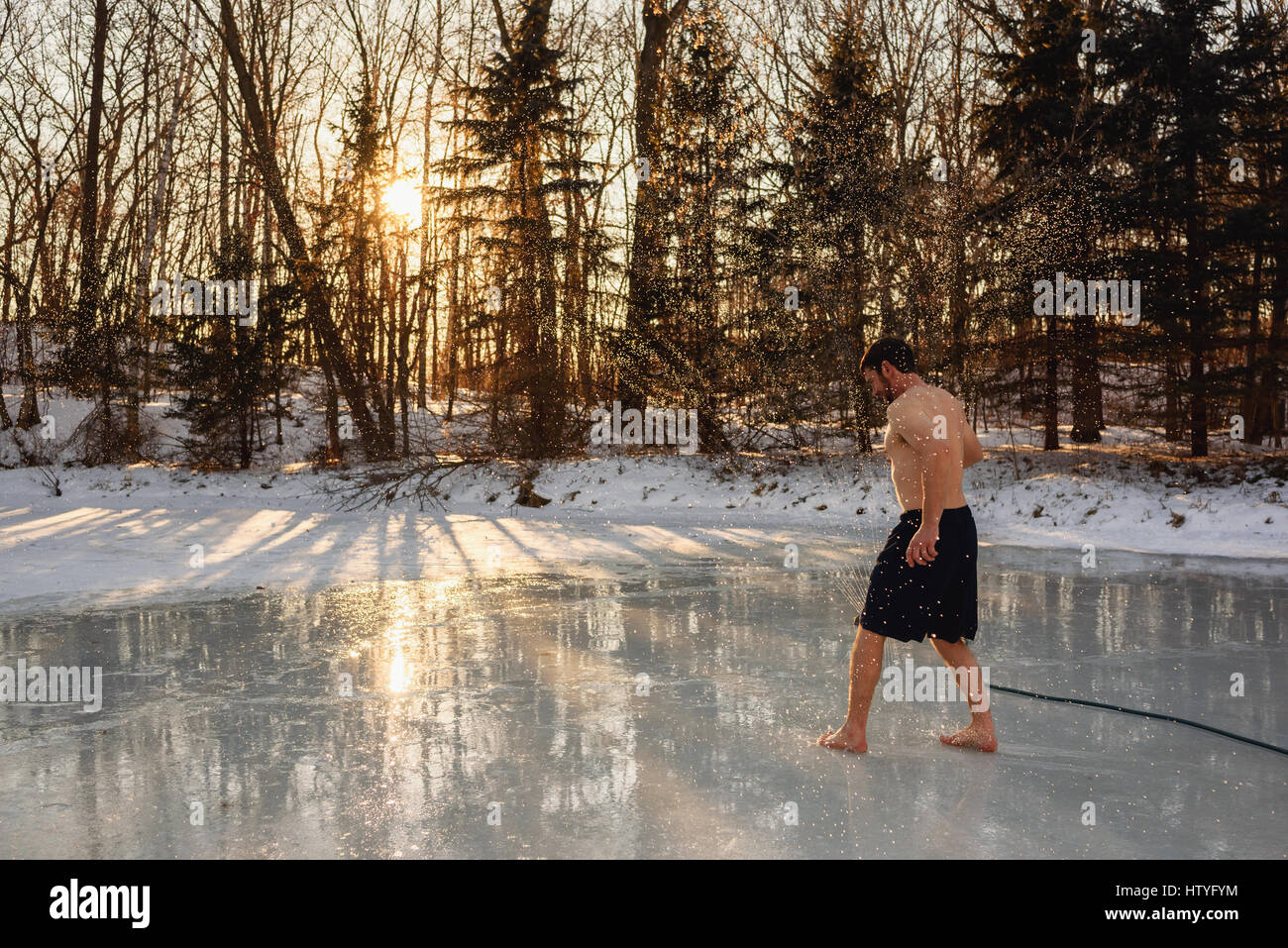 Mann in Badehose laufen durch Sprinkler auf zugefrorenen See Stockfoto