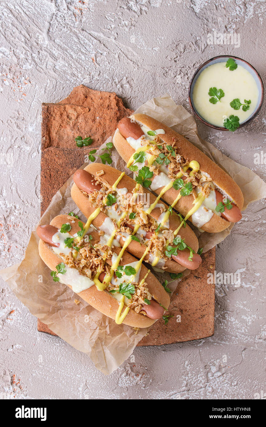 Hot Dogs mit Wurst, gebratenen Zwiebeln, Koriander, Käse-Sauce und Senf, serviert auf Terrakotta-Board über Beige Betontextur Hintergrund. FAS Stockfoto