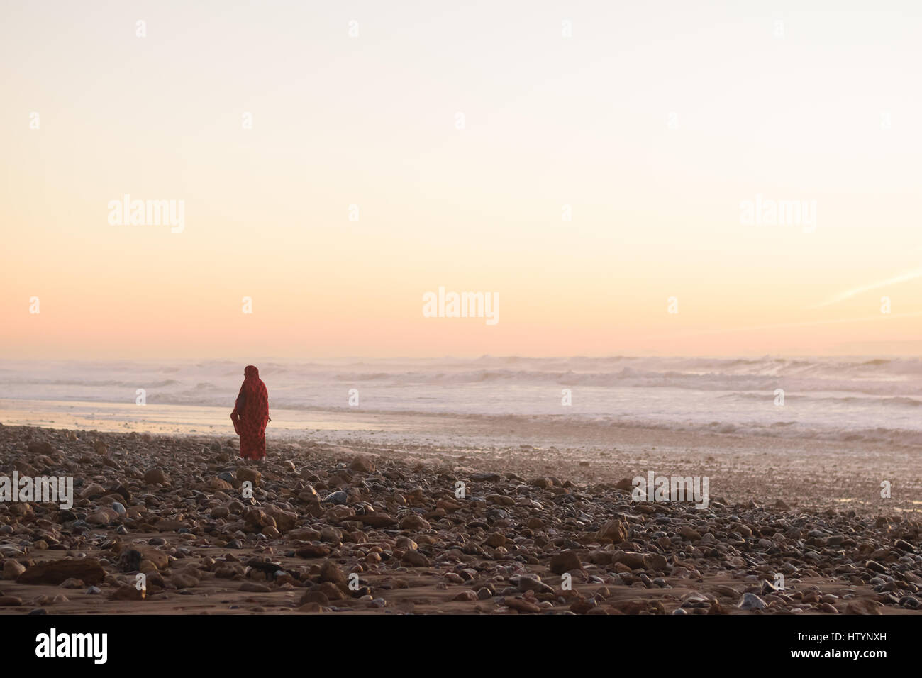 Eine Frau in einem roten Kleid zu Fuß am Strand bei Sonnenuntergang in Marokko. Stockfoto