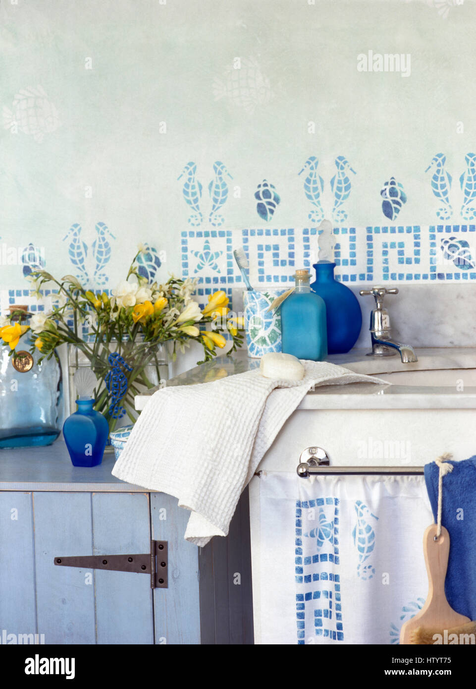 Schablonieren auf Wand über dem Waschbecken im Bad Wirtschaft mit einer Vase von Freesien auf einen gemalten blauen Schrank Stockfoto