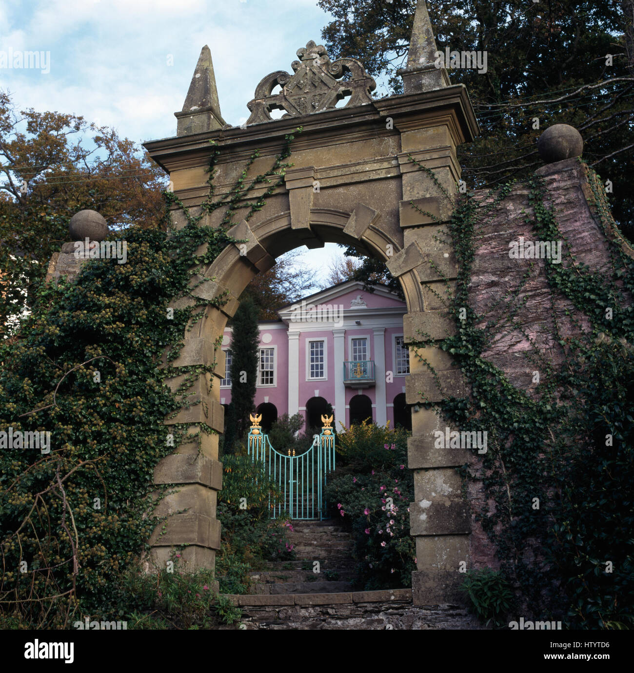 Blick durch ein großes Stein Tor ein blass grün lackierten Tor und ein Rosa Landhaus Stockfoto