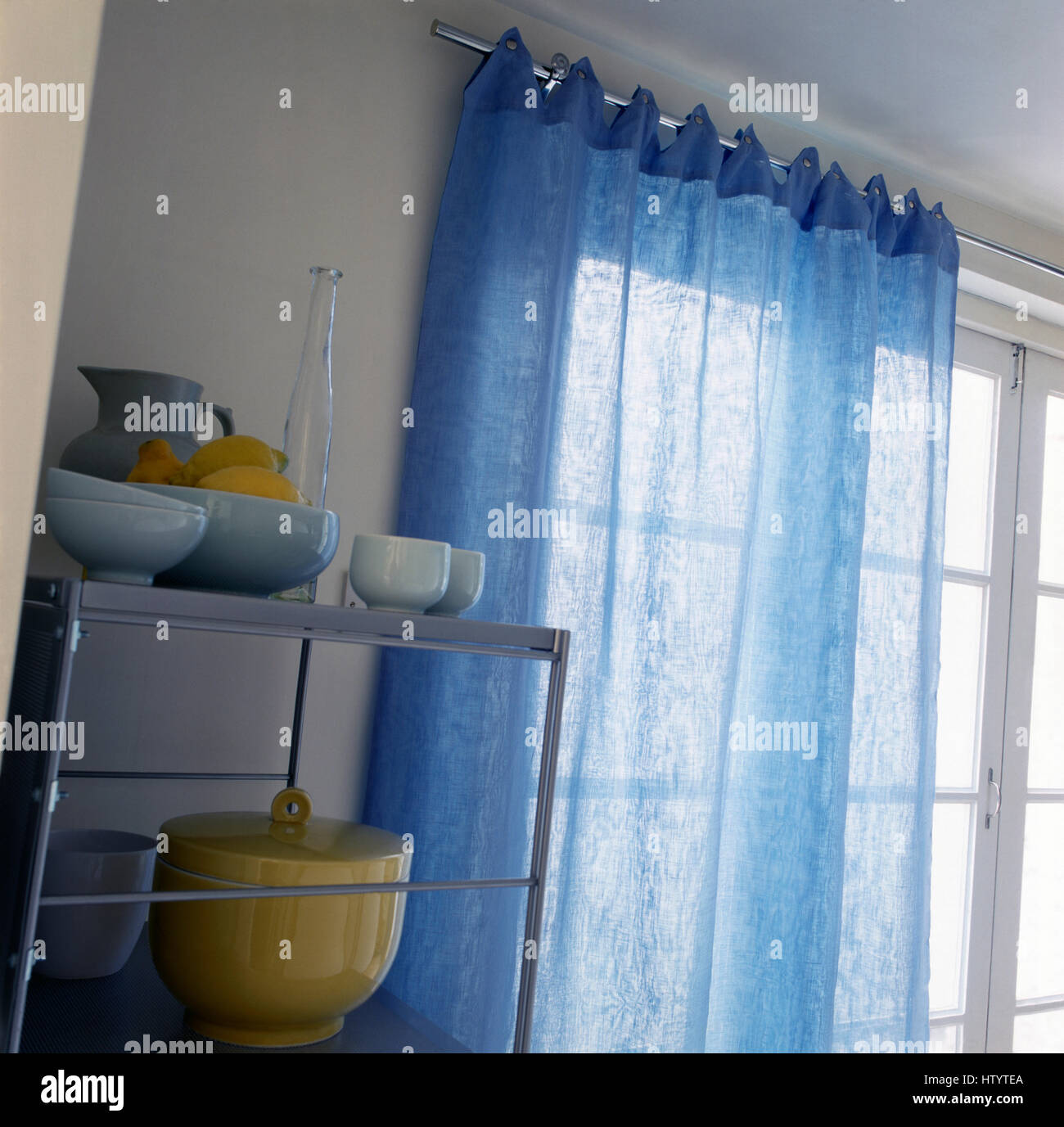Blaue Voile Vorhang auf einer Metallstange über Fenster neben Metallregale Stockfoto