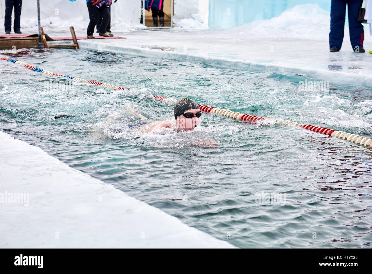 SAHYURTA, Gebiet IRKUTSK, Russland - März 11.2017: Cup des Baikalsees. Winter-Schwimmwettkampf. Ein Schwimmer bewegt sich sehr schnell in sehr kaltem Wasser in einen hol Stockfoto