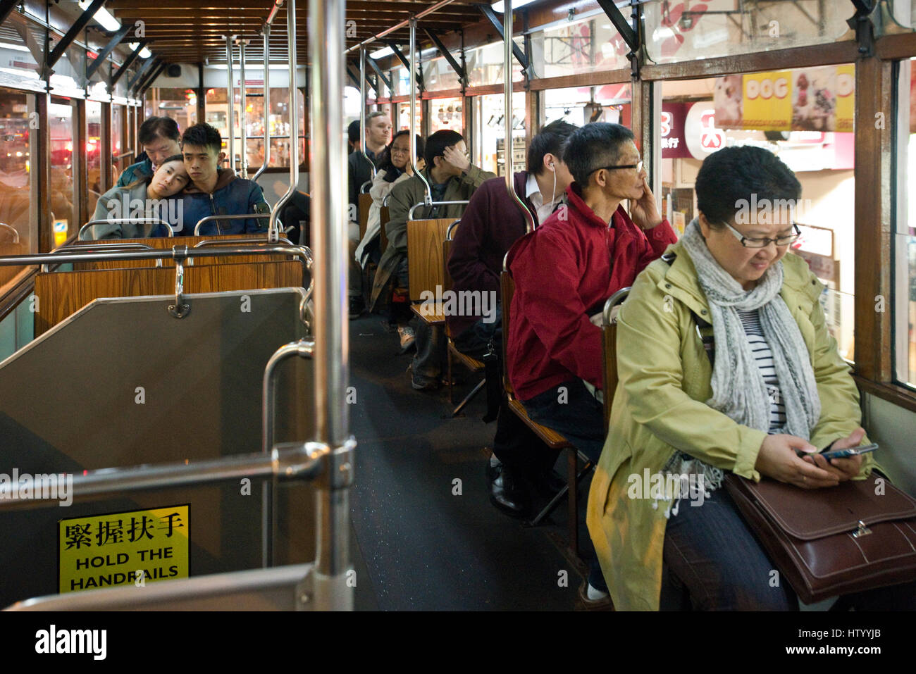 Passagiere sitzen in einer Straßenbahn Fahrt entlang einer Straße in Causeway Bay mit einer Frau, die ihr Handy überprüfen. Stockfoto