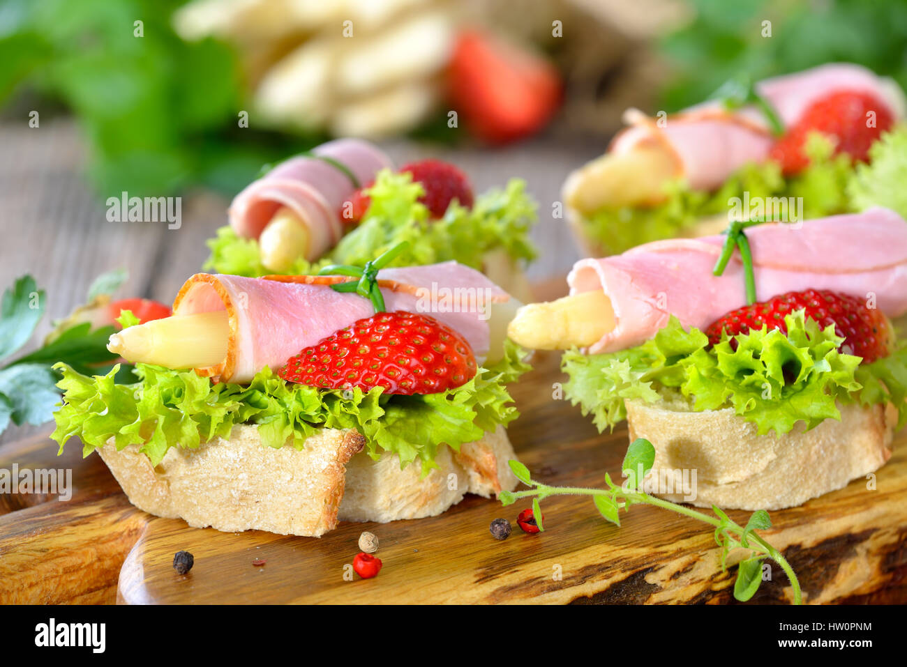 Köstliche Häppchen mit Schinken Brötchen und weißer Spargel mit frischen Erdbeeren auf knusprigem Baguette mit Blätter Lollo bionda Stockfoto