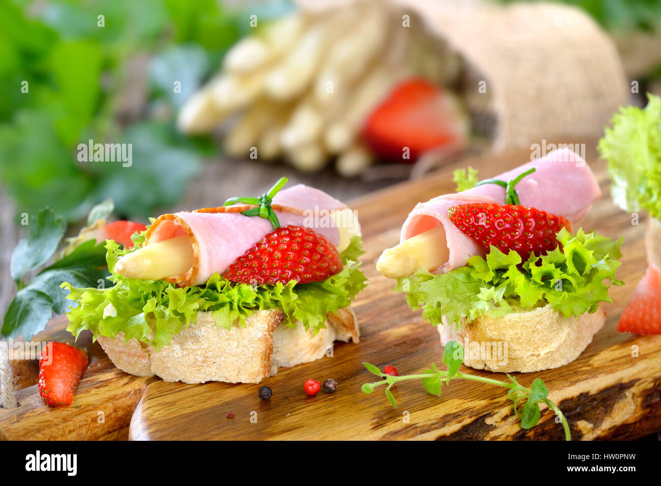 Köstliche Häppchen mit Schinken Brötchen und weißer Spargel mit frischen Erdbeeren auf knusprigem Baguette mit Blätter Lollo bionda Stockfoto