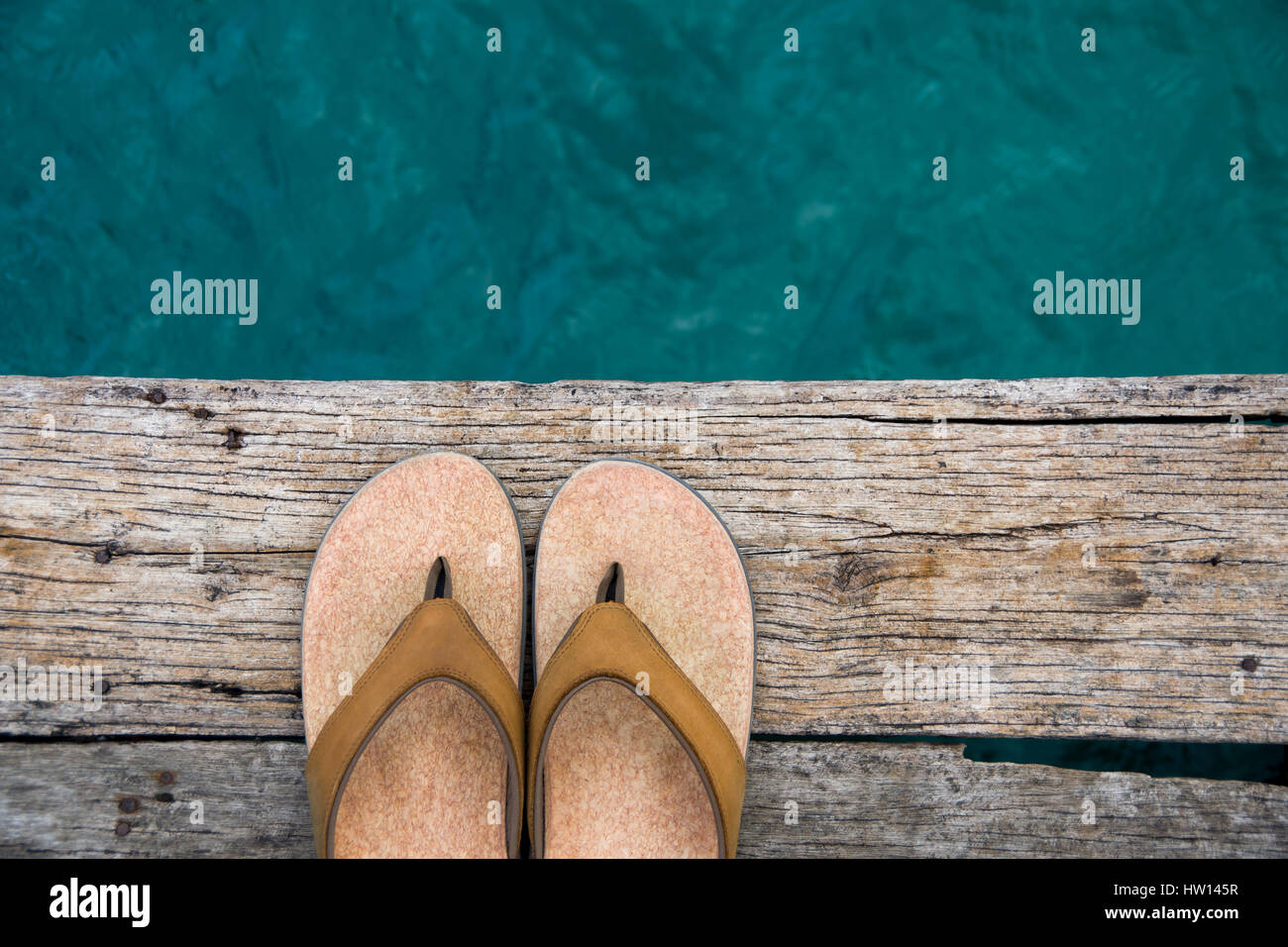 Beige Flip-flop-Sandalen am Rand des hölzernen Dock über Wasser Stockfoto