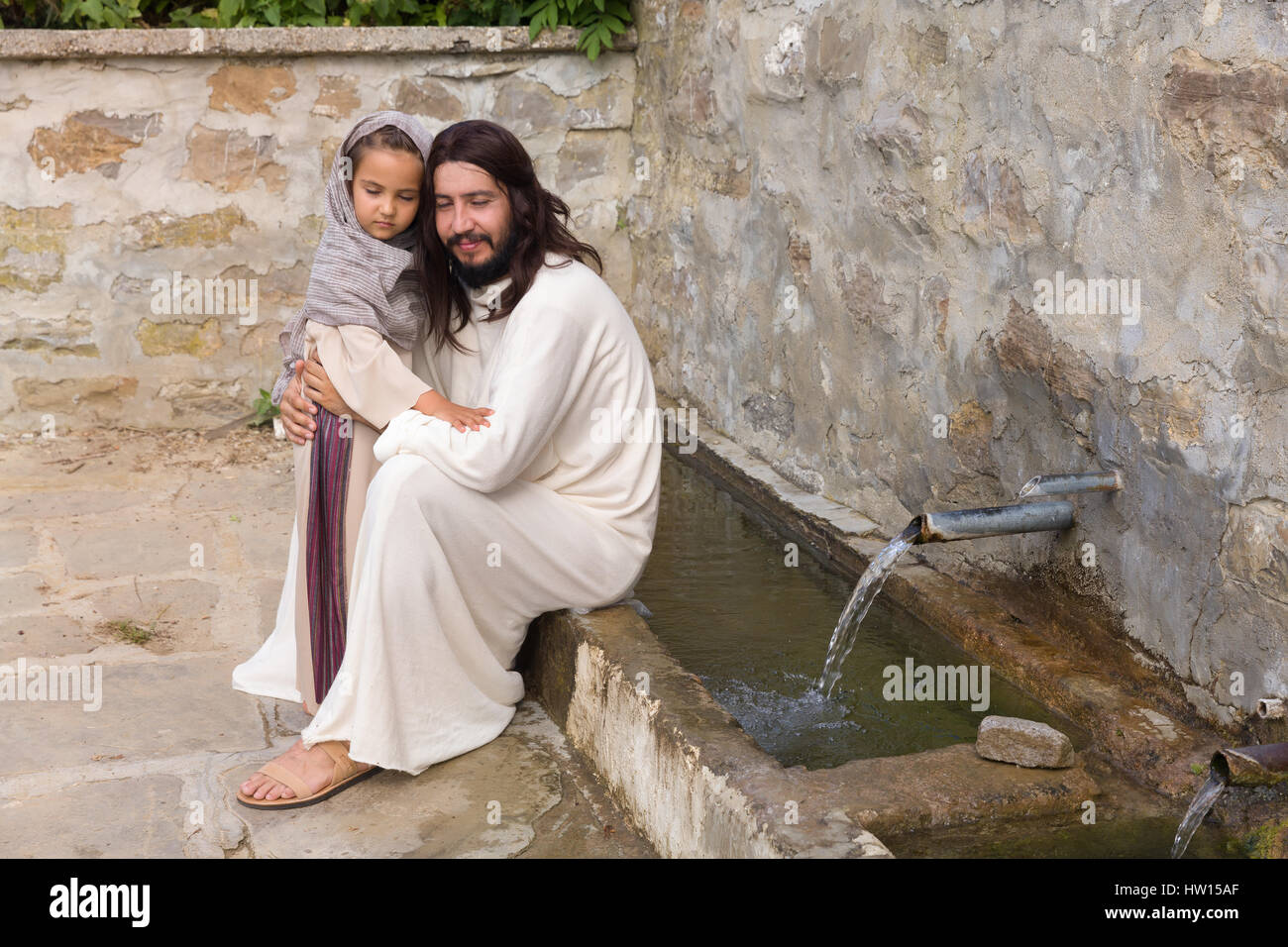 Biblische Szene, in der Jesus sagt: Lasst die Kinder kommen zu mir, ein kleines Mädchen Segen. Historisches Reenactment an einem alten Brunnen. Stockfoto