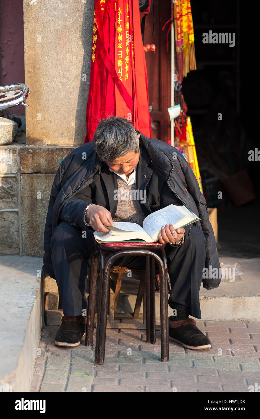 TAI'an, China - JAN 2014 - Ein alter chinesischer Mann liest vor seinem Geschäft in der Stadt Tai'an, Provinz Shandong, China Stockfoto