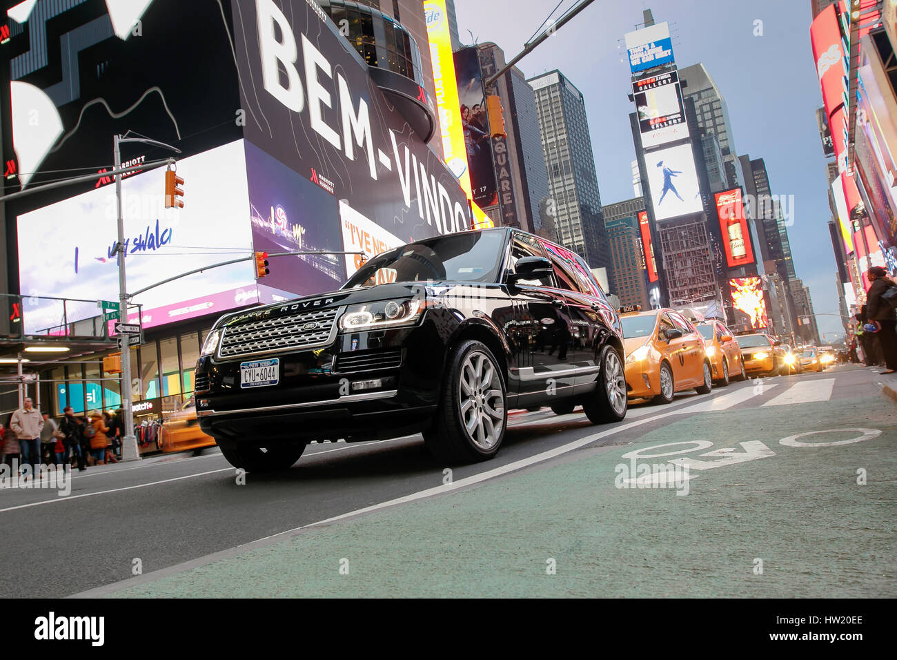 Ein Range Rover SUV und eine Zeichenkette von Yellow Cabs dahinter sind im Verkehr am Broadway an Times Square zu sehen. Stockfoto
