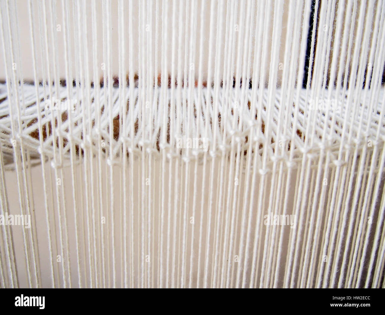 Viele weiße Fäden auf einem Webstuhl bilden eine helle, angenehme Muster. Stockfoto