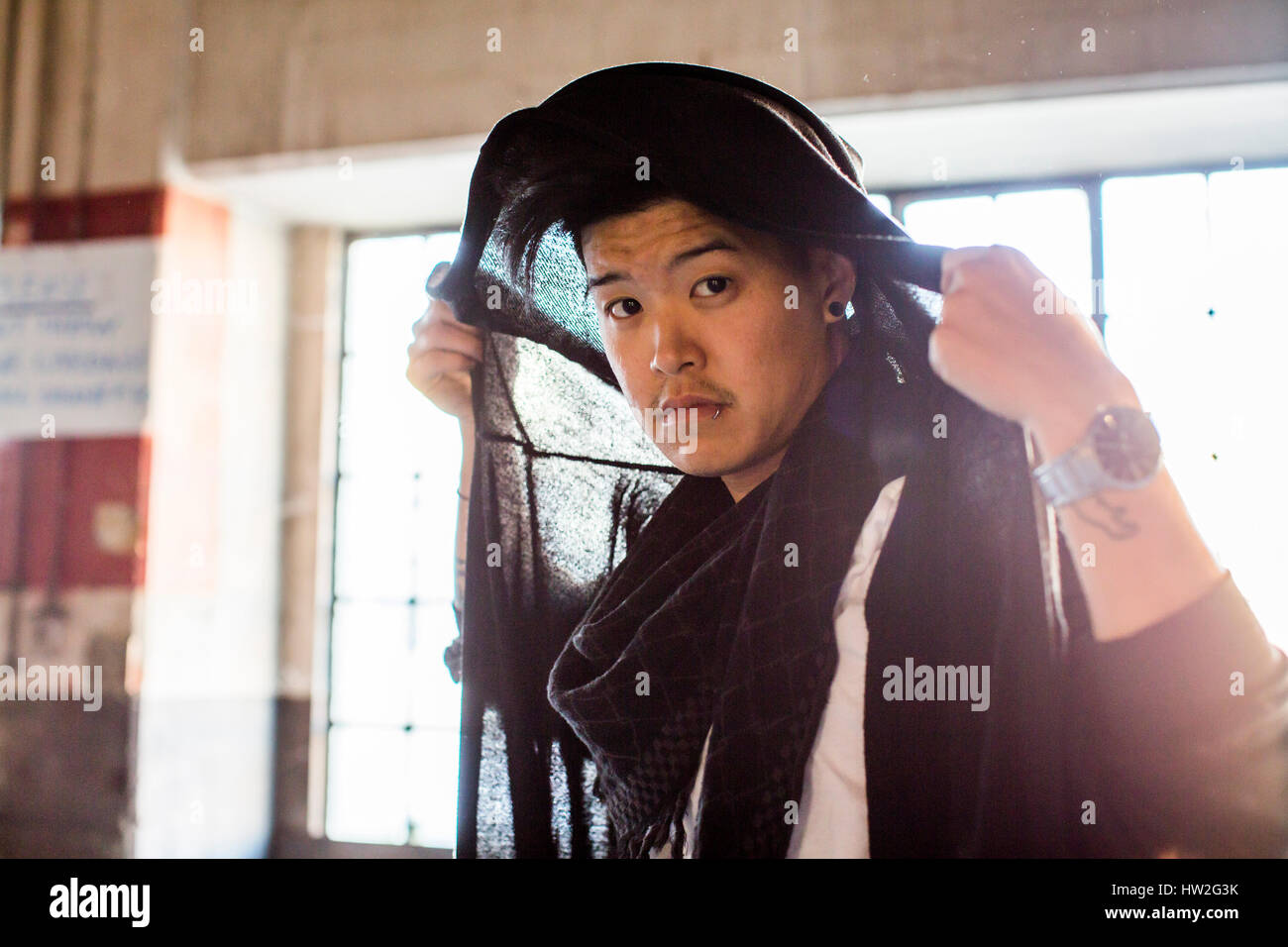 Androgyne asiatischer Mann halten Schal auf Kopf Stockfoto