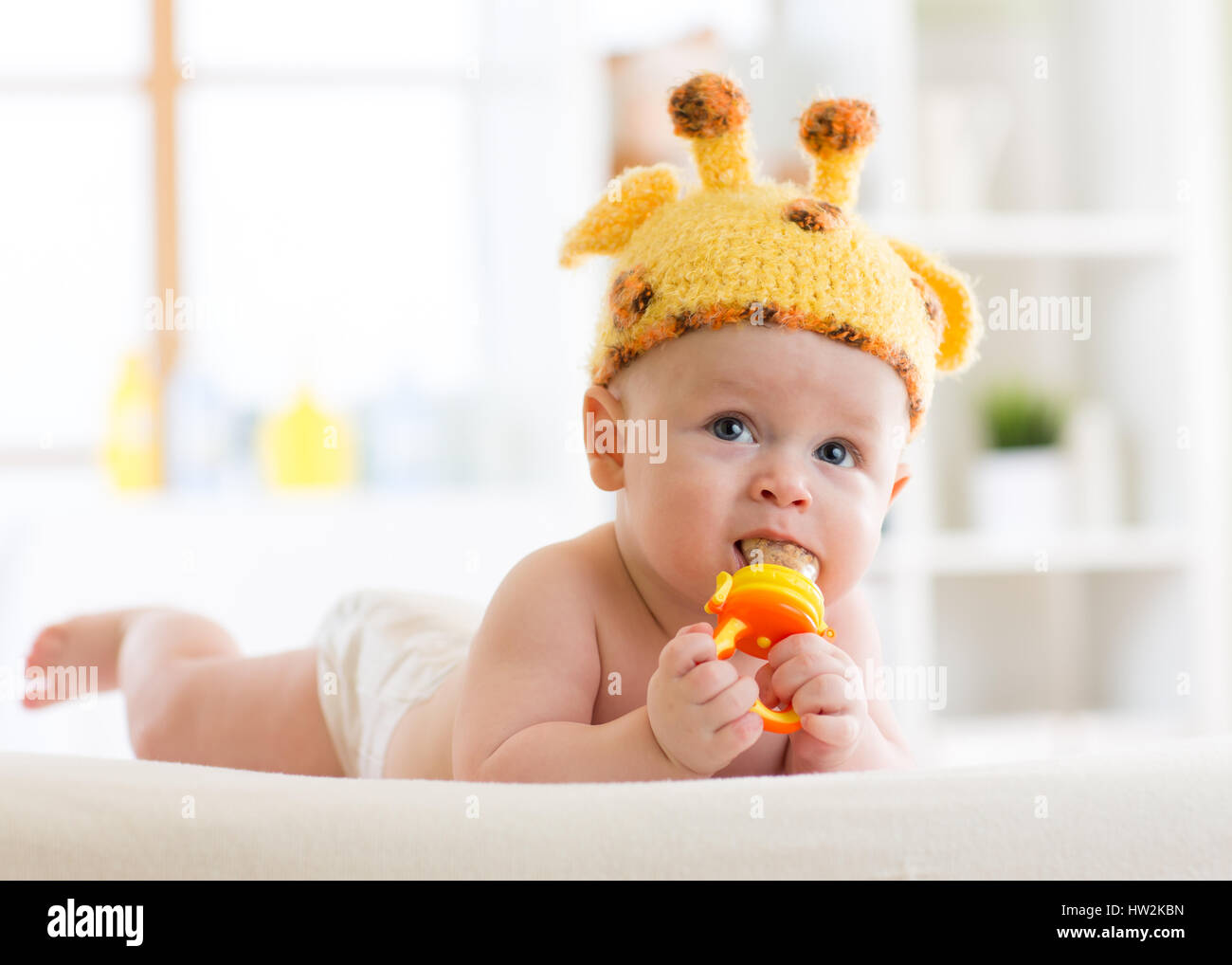 Lustige Baby junge Giraffe Hut liegen auf dem Bauch im Kindergarten. Kleines Kind mit Knabber-Spielzeug. Stockfoto