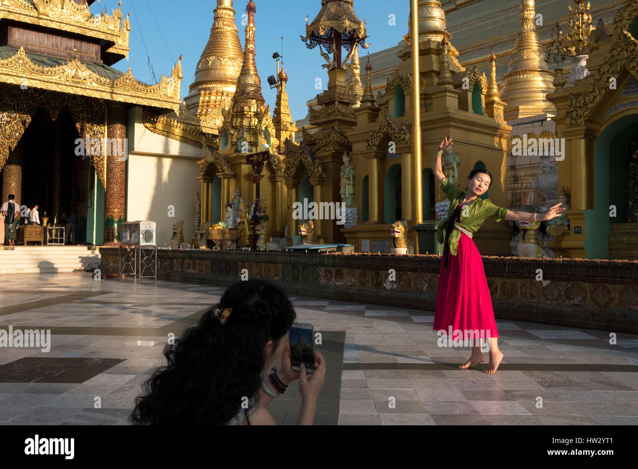 Eine Frau wirft in einem Tanz, während sie auf dem Handy an der Shwedagon-Pagode in Yangon, Region Yangon, Myanmar gefilmt wird Stockfoto