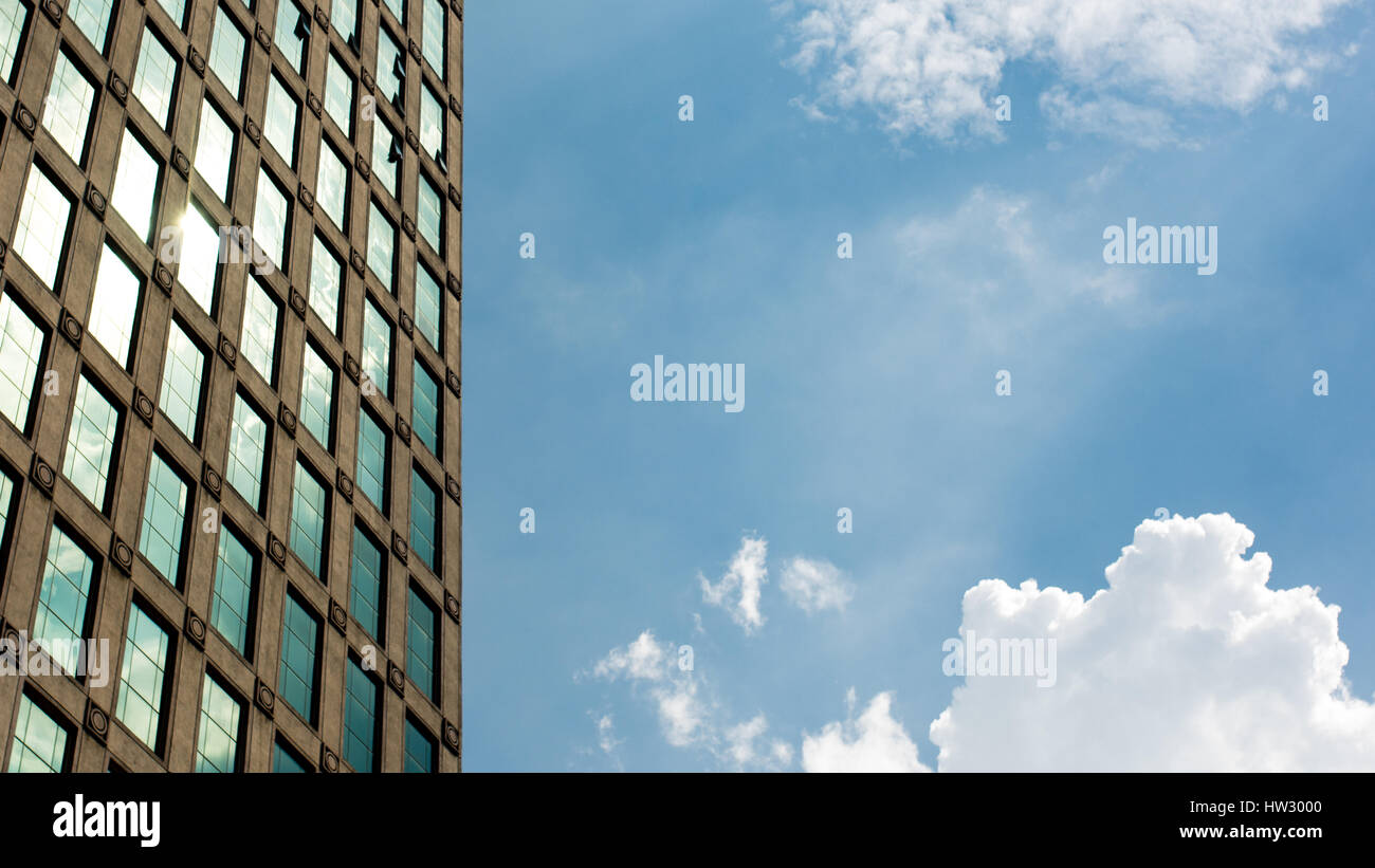 Die helle Sonne an einem sonnigen Sommertag Reflexion aus dem Glas eine Gebäude-Fassade mit weißen Wölkchen am Himmel. Stockfoto