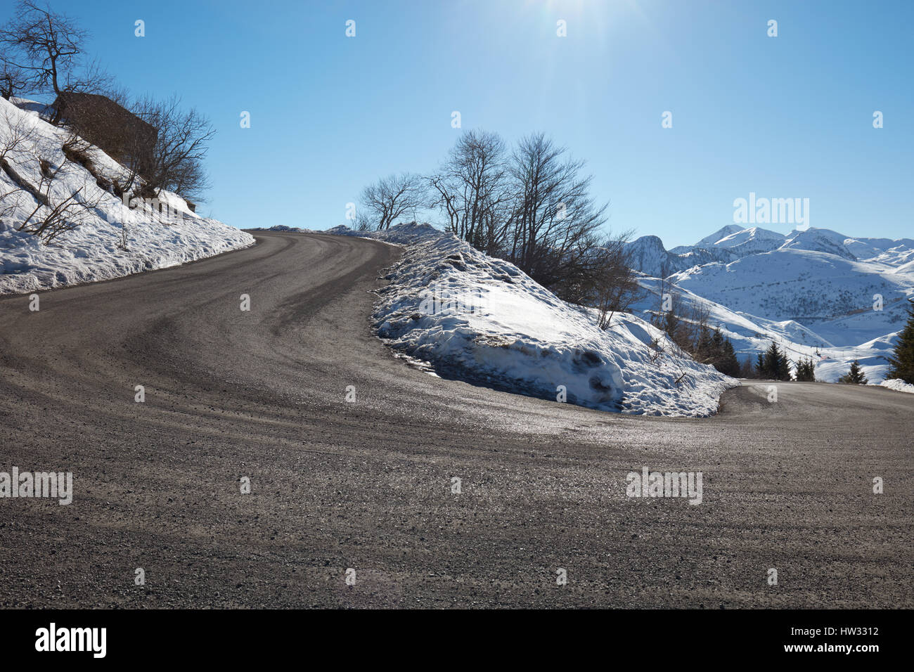 Leere Bergstraße mit Kurve in einem verschneiten Winter, blauen Himmel an einem sonnigen Tag Stockfoto