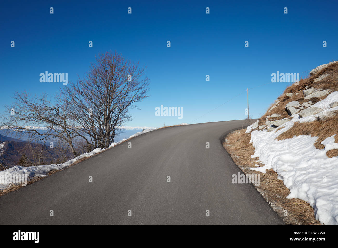 Leere alpine Bergstraße mit Schnee auf Seiten, blauen Himmel an einem sonnigen Tag Stockfoto