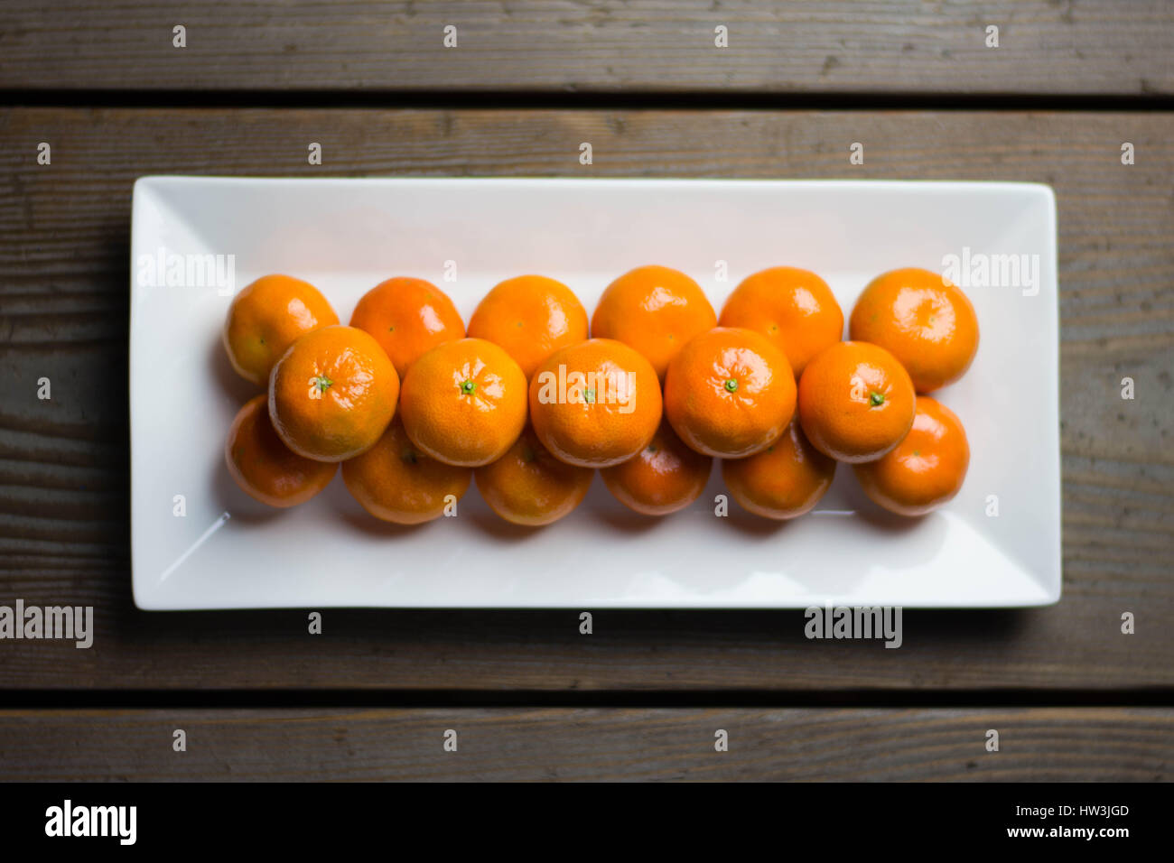 Mandarinen symmetrisch aufgereiht auf weißen Teller mit rustikalen Tisch im Hintergrund. Stockfoto