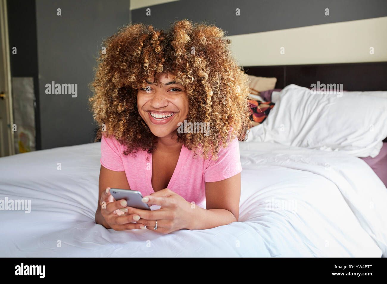 Lächelnde schwarze Frau auf Bett SMS auf Handy Stockfoto