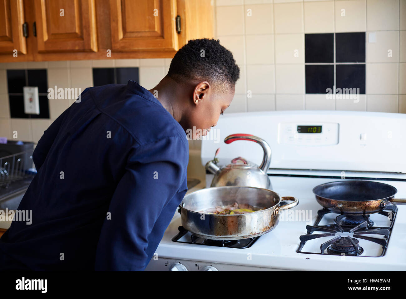 Schwarze Frau riechende Lebensmittel in Pfanne auf Herd kochen Stockfoto